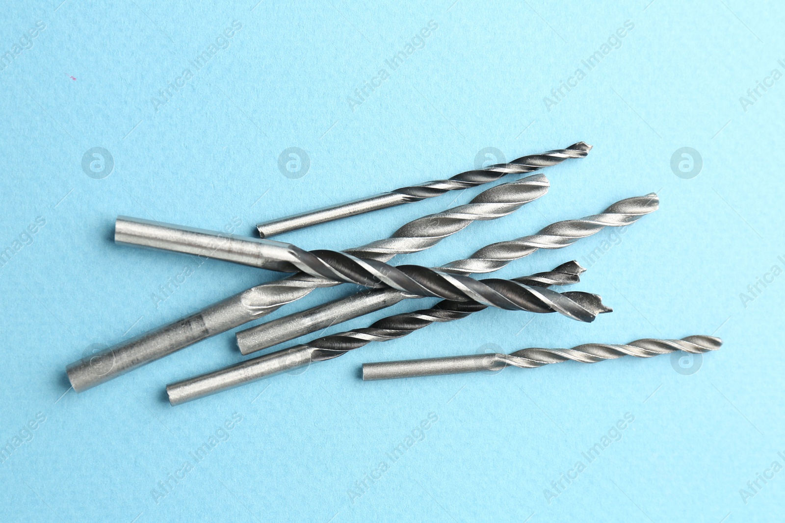 Photo of Many different drill bits on light blue background, top view