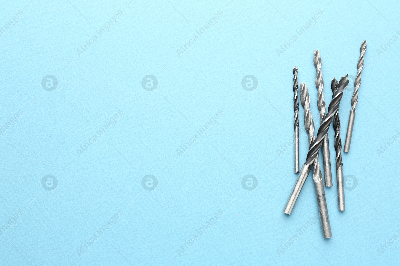 Photo of Many different drill bits on light blue background, top view. Space for text