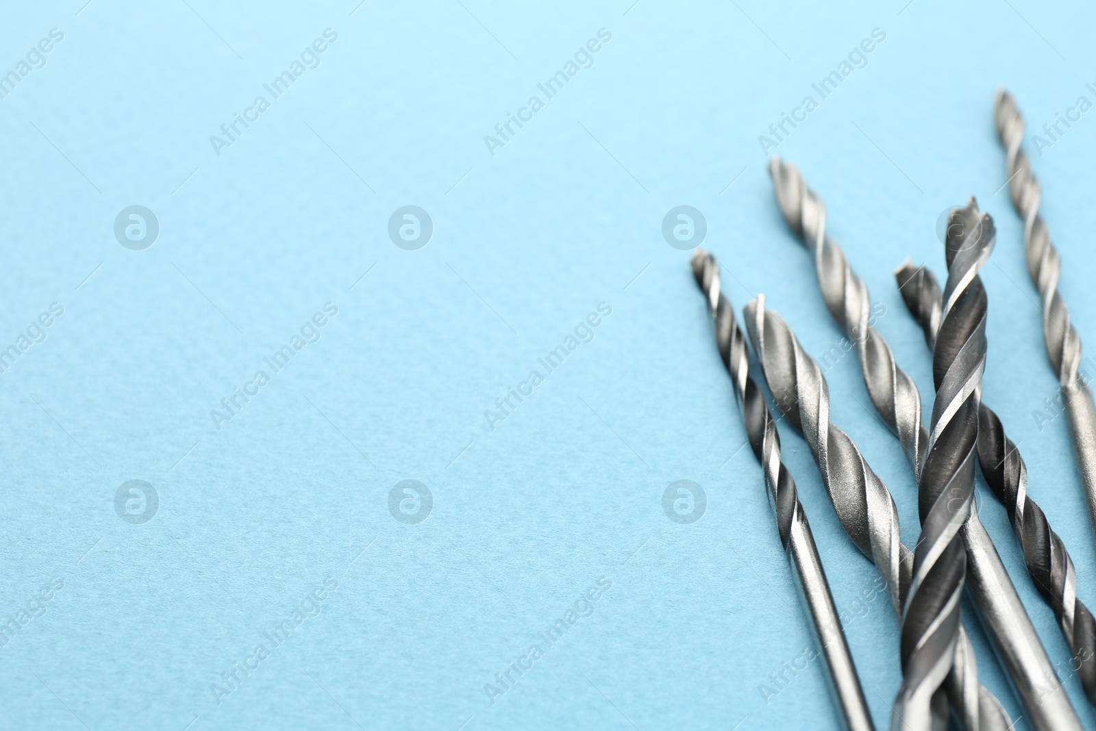 Photo of Many different drill bits on light blue background, top view. Space for text