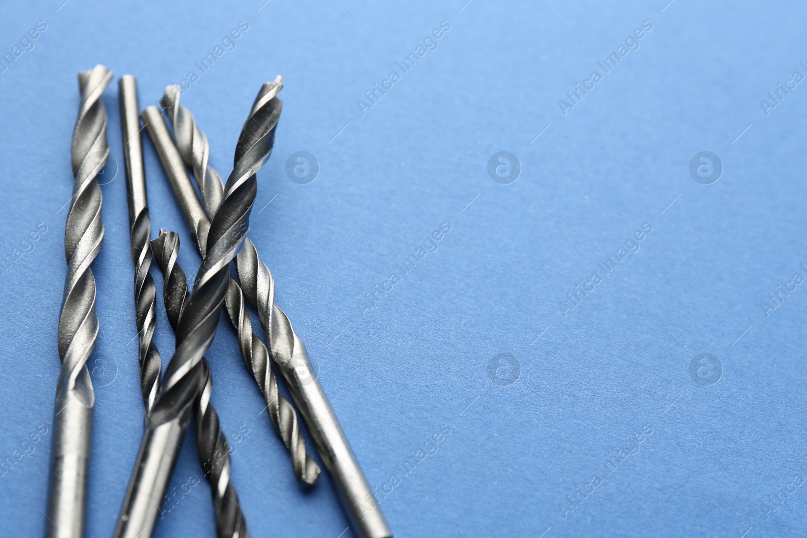 Photo of Many different drill bits on light blue background, space for text