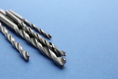 Photo of Many different drill bits on light blue background, closeup. Space for text