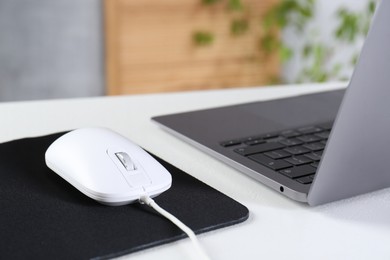 Photo of Computer mouse with mousepad and laptop on white table indoors, closeup