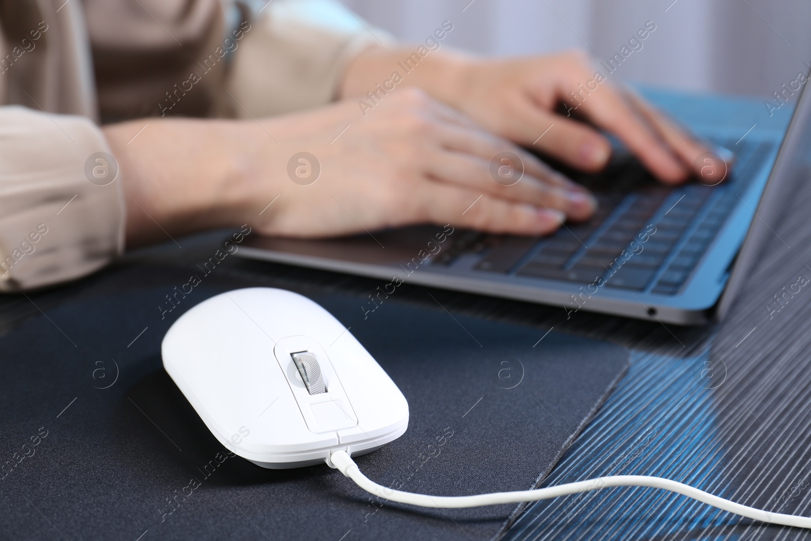 Photo of Woman working with laptop at black wooden table, focus on computer mouse