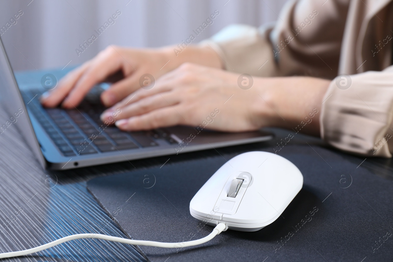 Photo of Woman working with laptop at black wooden table, focus on computer mouse