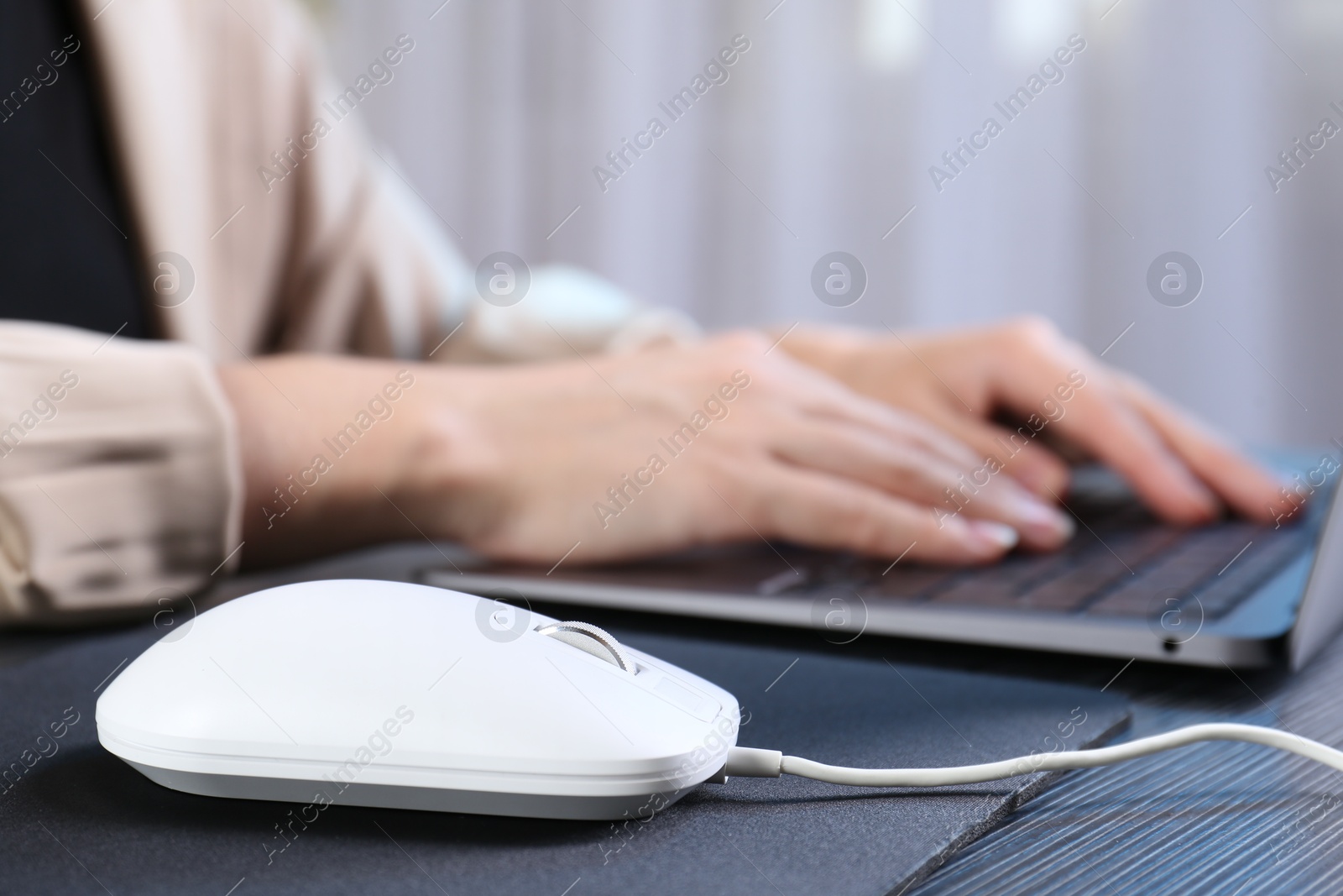 Photo of Woman working with laptop at black wooden table, focus on computer mouse