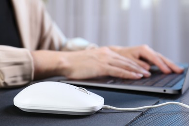 Photo of Woman working with laptop at black wooden table, focus on computer mouse