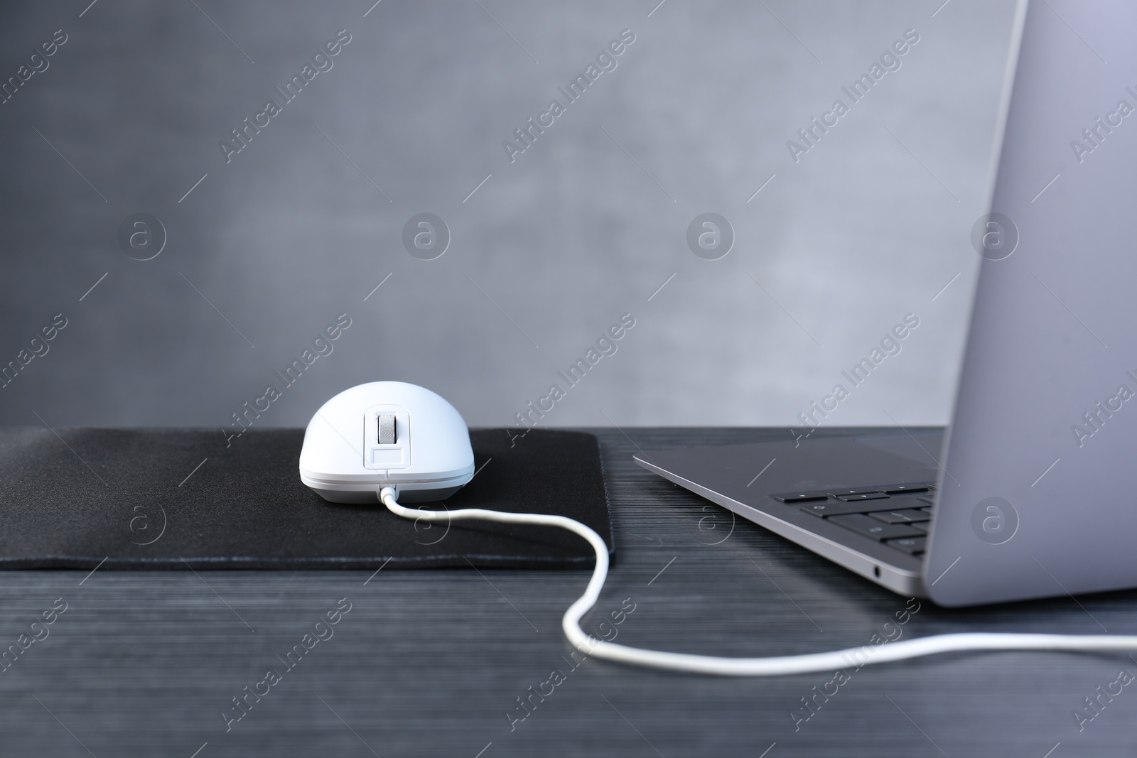 Photo of White computer mouse with mousepad and laptop on black wooden table