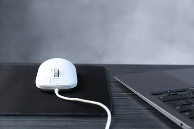 Photo of White computer mouse with mousepad and laptop on black wooden table, closeup