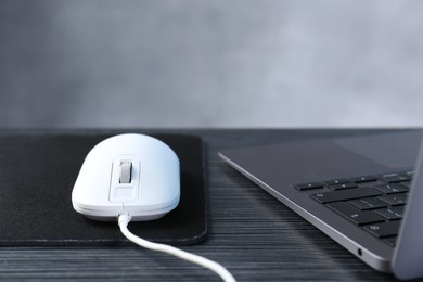 Photo of White computer mouse with mousepad and laptop on black wooden table, closeup