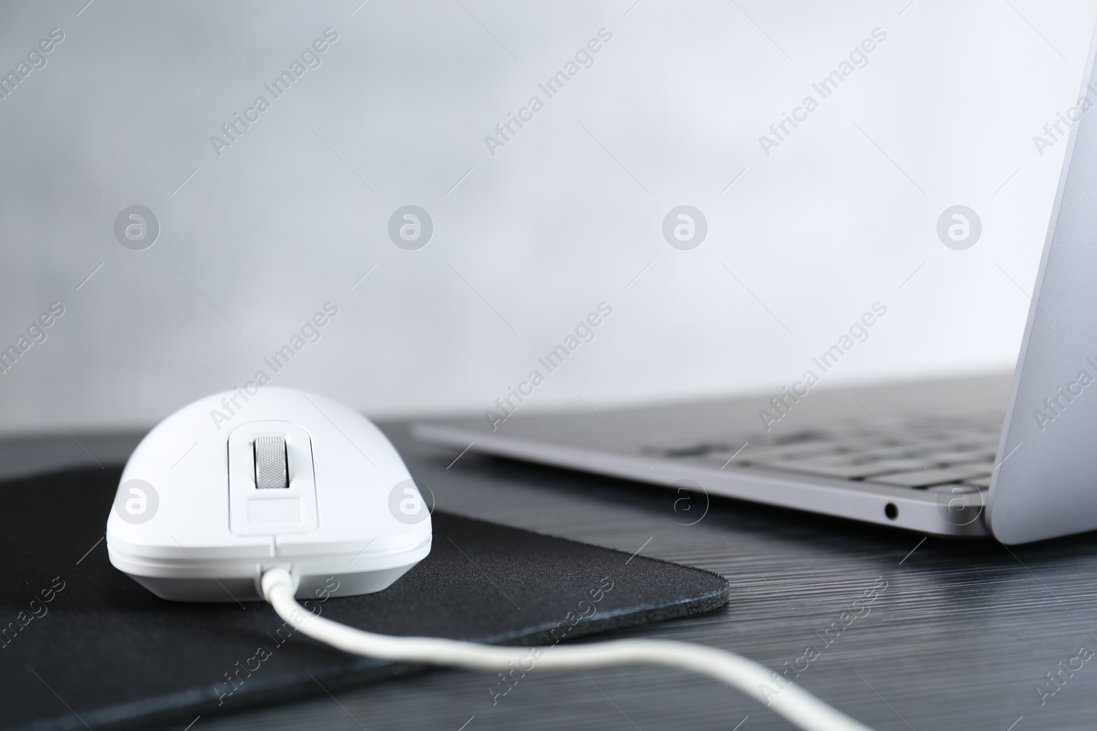 Photo of White computer mouse with mousepad and laptop on black wooden table, closeup