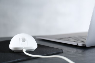 Photo of White computer mouse with mousepad and laptop on black wooden table, closeup