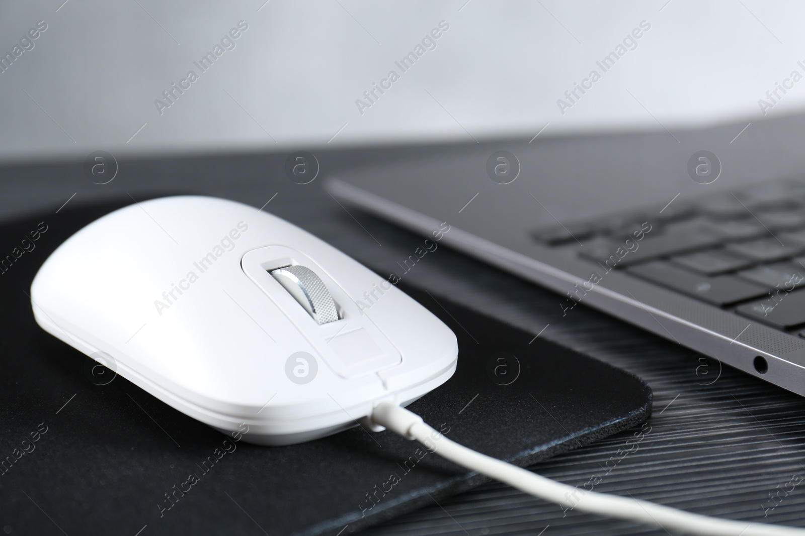 Photo of White computer mouse with mousepad and laptop on black wooden table, closeup