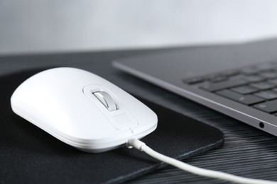 Photo of White computer mouse with mousepad and laptop on black wooden table, closeup