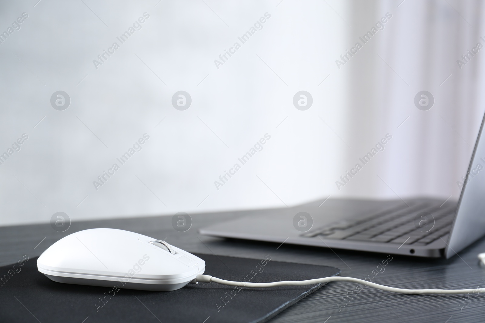 Photo of White computer mouse with mousepad and laptop on black wooden table, closeup