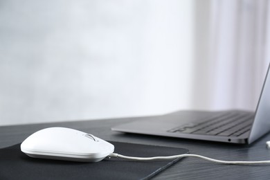 Photo of White computer mouse with mousepad and laptop on black wooden table, closeup