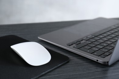 Photo of White computer mouse with mousepad and laptop on black wooden table, closeup