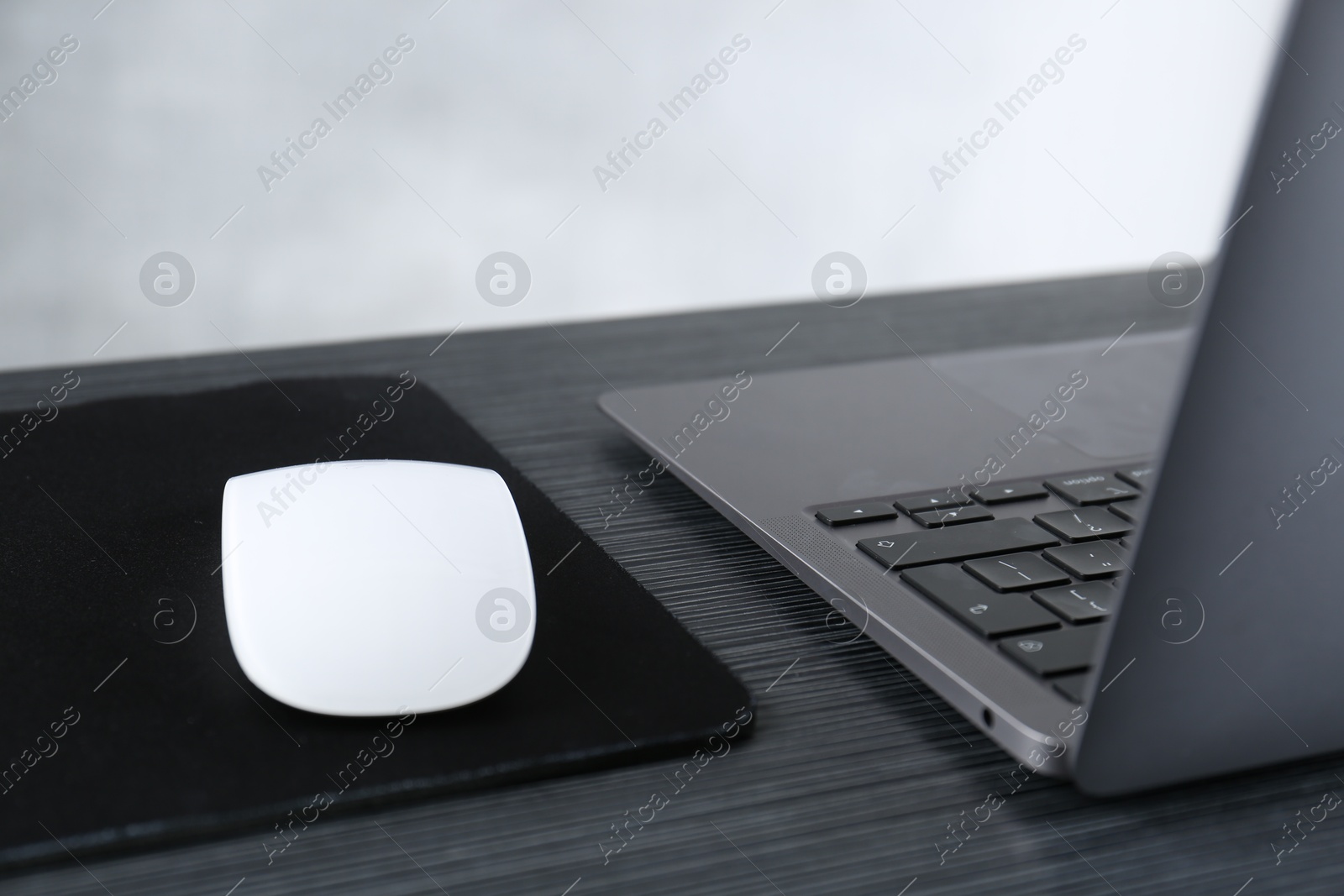 Photo of White computer mouse with mousepad and laptop on black wooden table