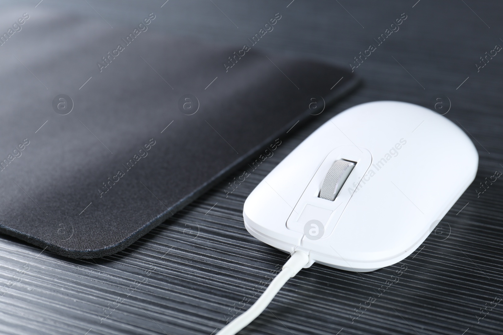 Photo of White computer mouse with mousepad on black wooden table, closeup