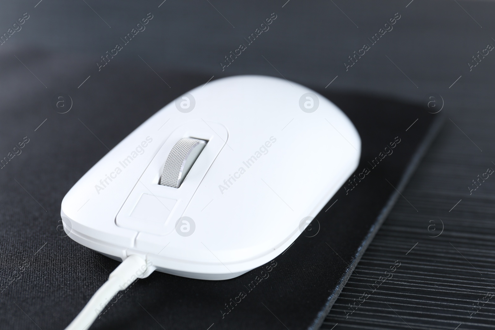 Photo of White computer mouse with mousepad on black wooden table, closeup