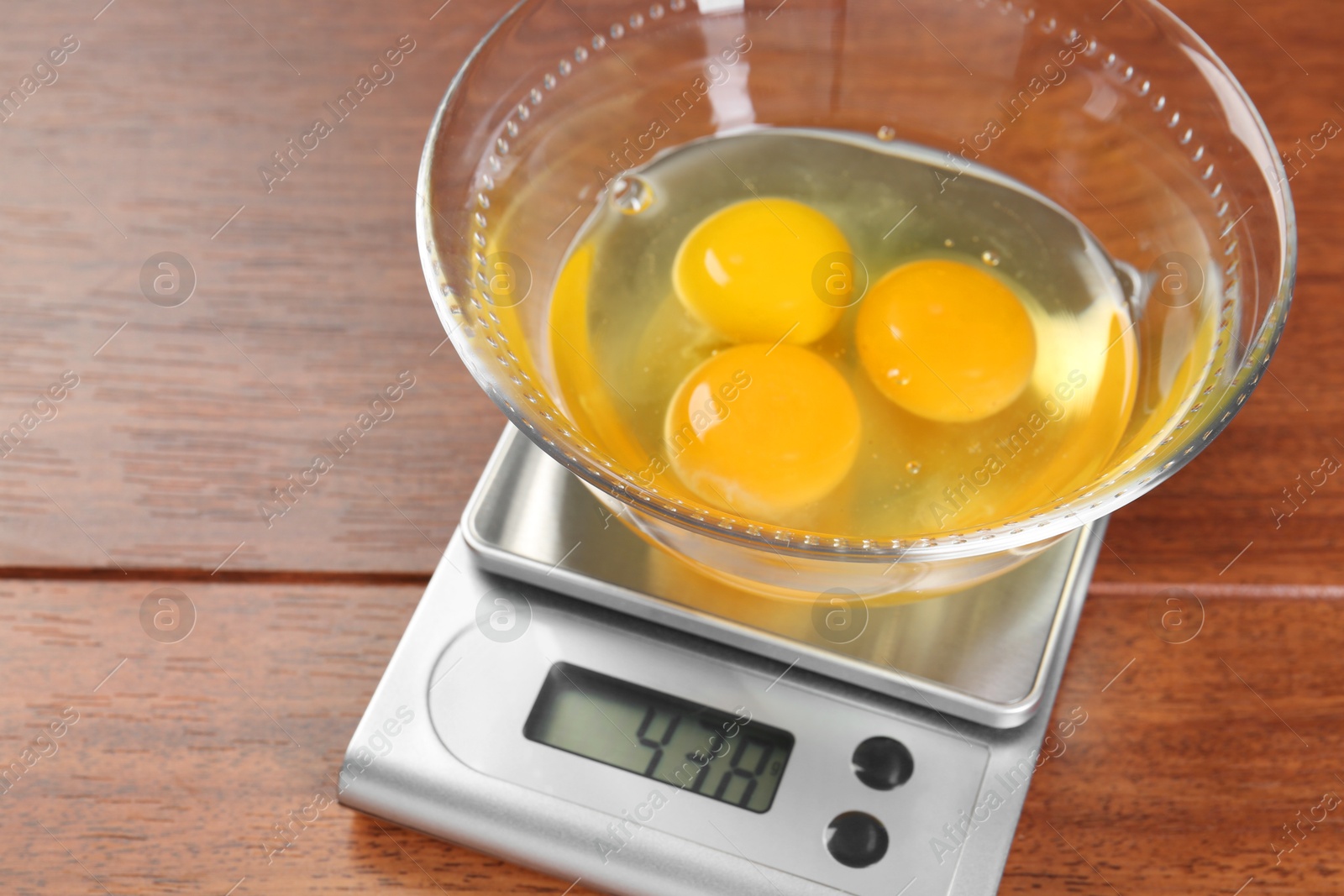 Photo of Kitchen scale with bowl of raw eggs on wooden table, closeup