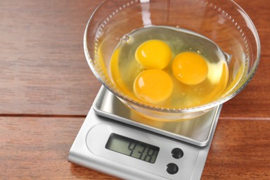 Kitchen scale with bowl of raw eggs on wooden table, closeup