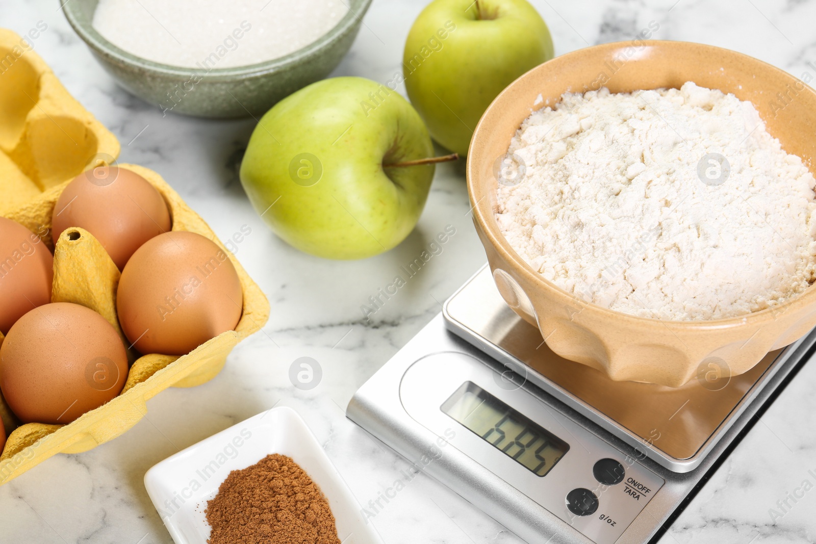 Photo of Kitchen scale with bowl of flour and products on white marble table, closeup