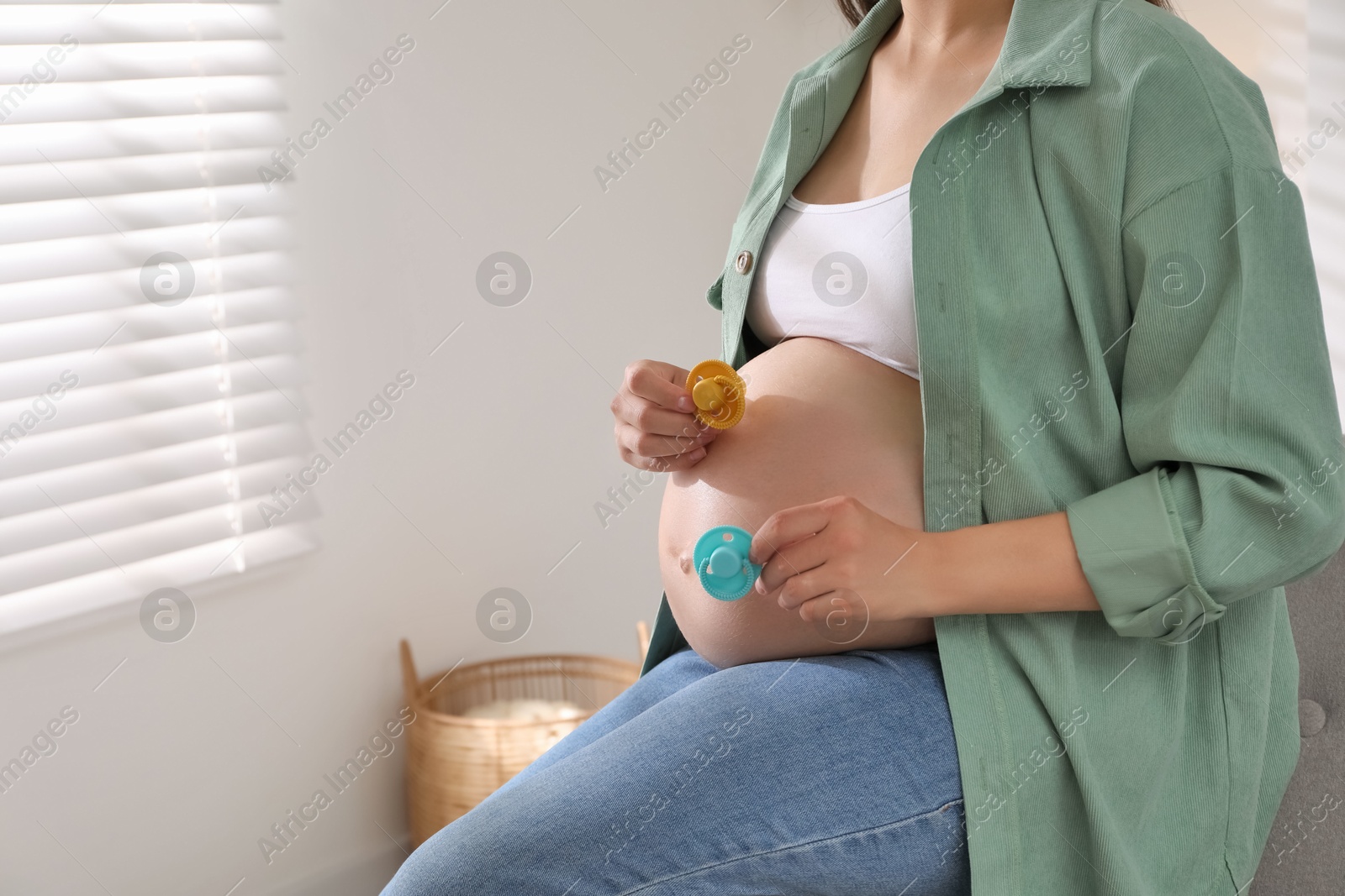 Photo of Pregnant woman with pacifiers at home, closeup. Expecting twins