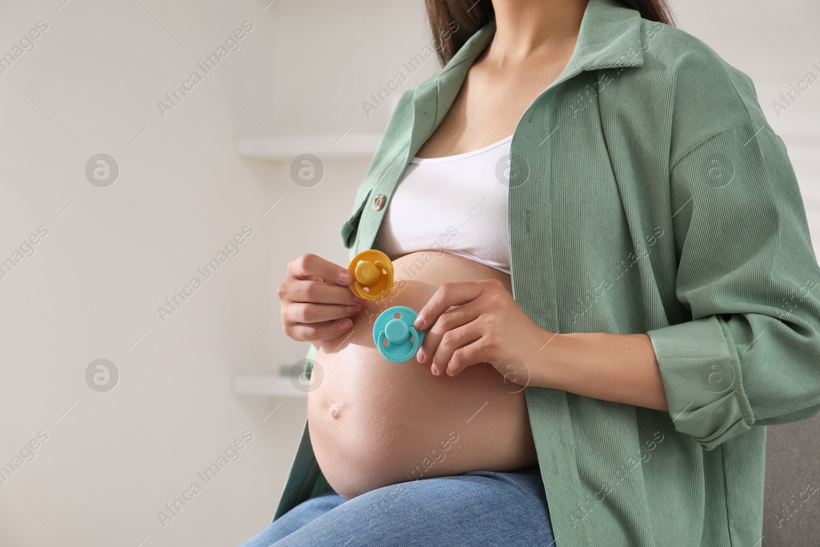 Photo of Pregnant woman with pacifiers at home, closeup and space for text. Expecting twins