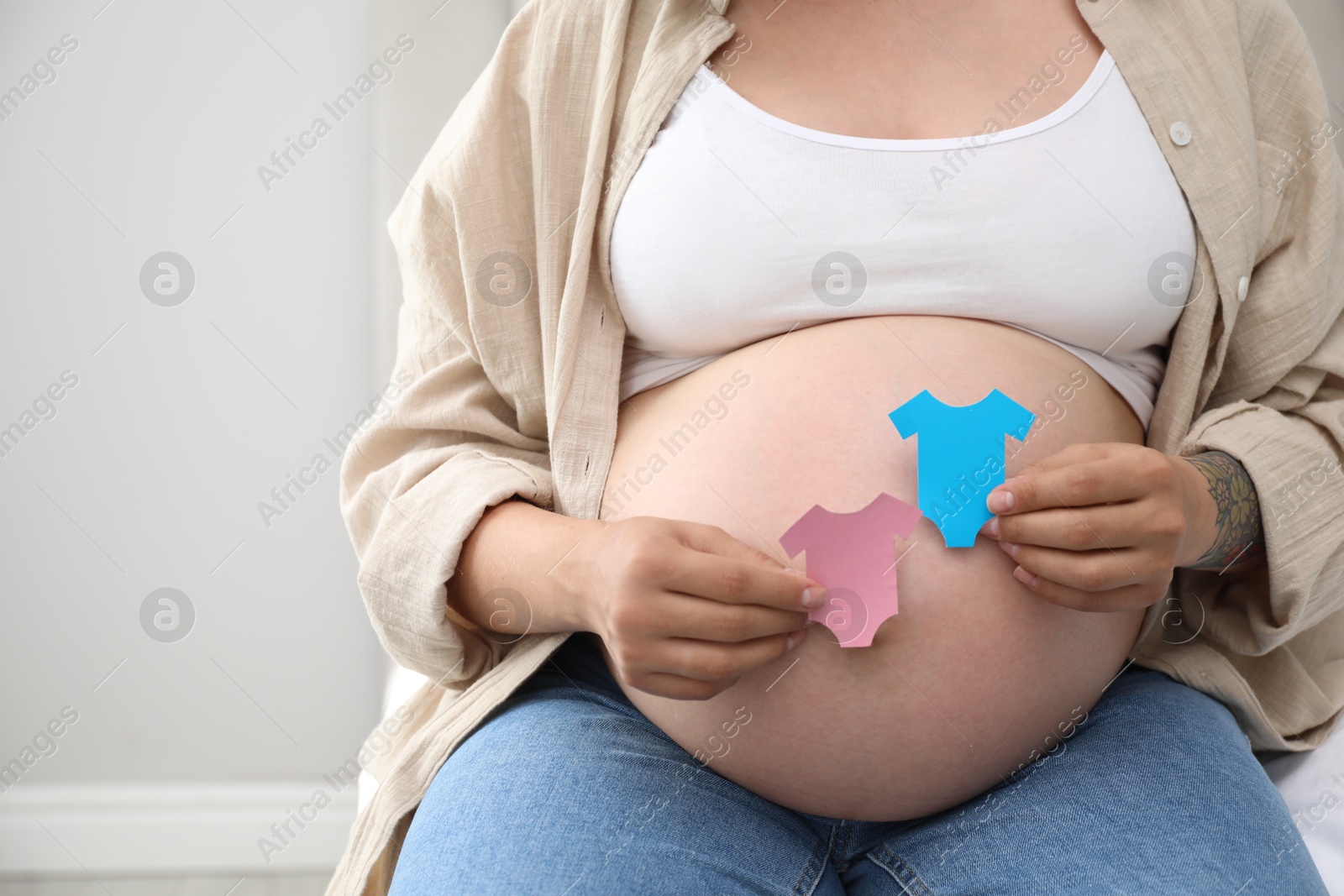 Photo of Pregnant woman with paper T-shirts on light gray background, closeup. Expecting twins