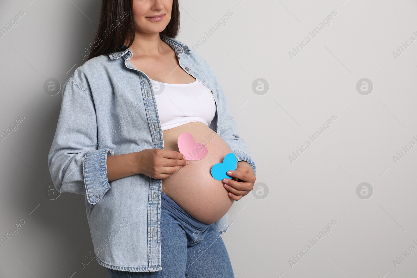 Photo of Pregnant woman with paper hearts on light gray background, closeup and space for text. Expecting twins