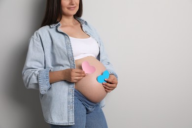 Pregnant woman with paper hearts on light gray background, closeup and space for text. Expecting twins