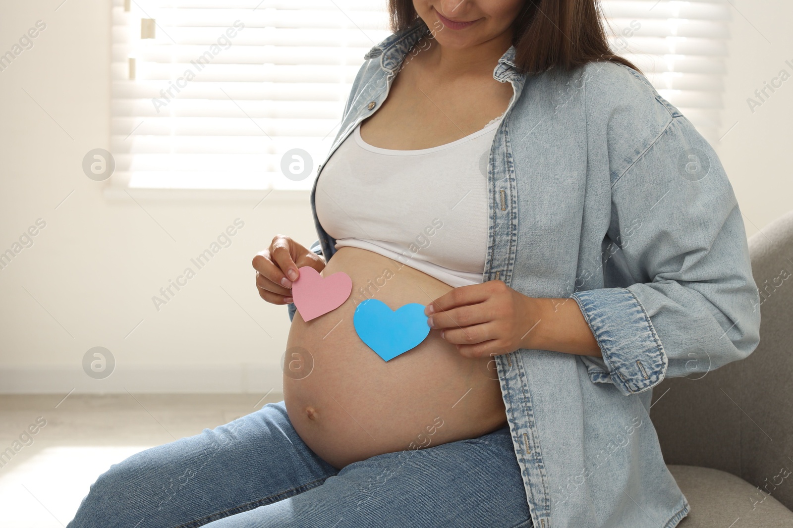 Photo of Pregnant woman with paper hearts on sofa at home, closeup. Expecting twins