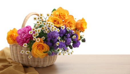 Wicker basket with beautiful flowers on wooden table against white background, space for text