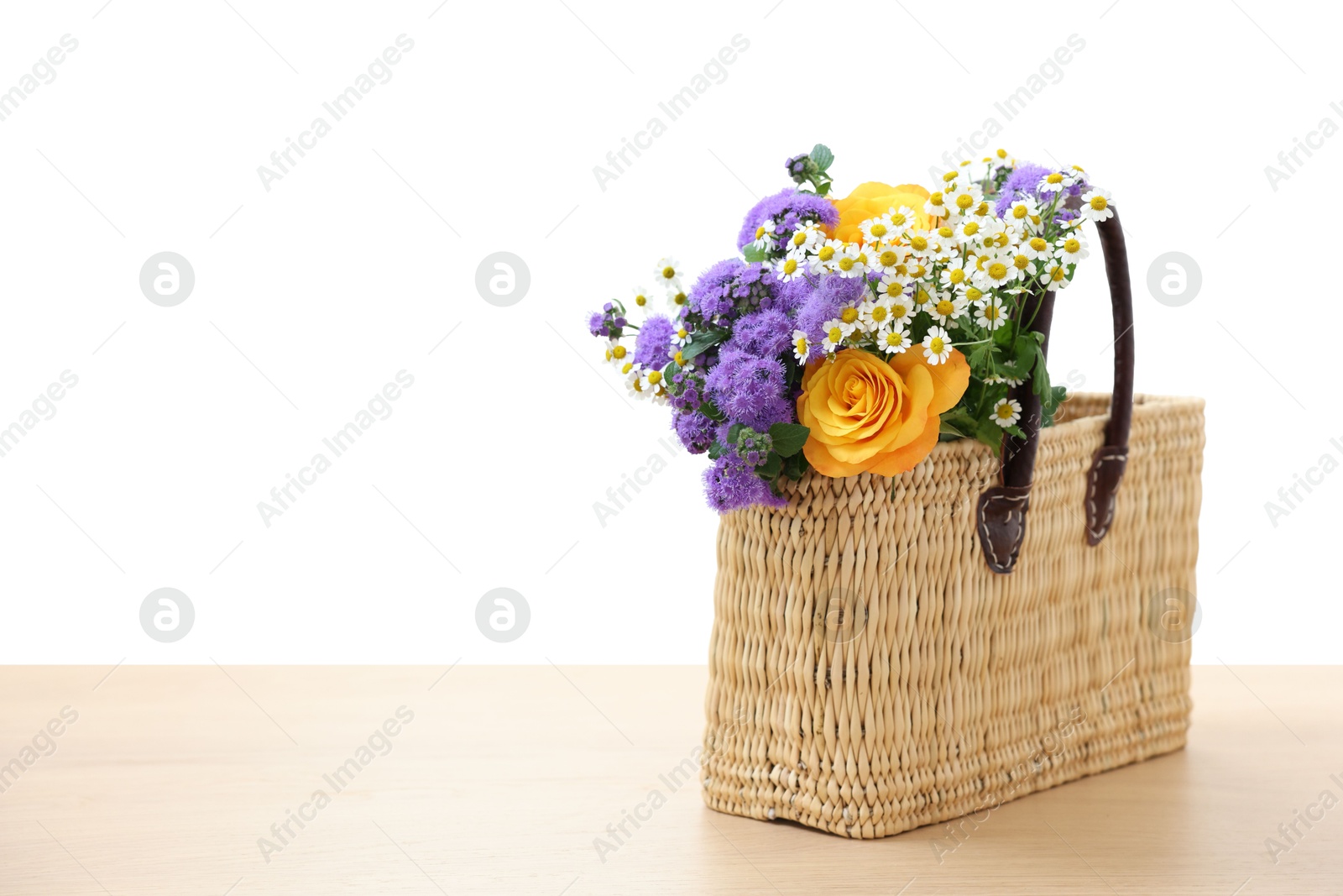 Photo of Wicker basket with beautiful flowers on light wooden table, space for text