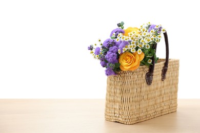 Photo of Wicker basket with beautiful flowers on light wooden table, space for text