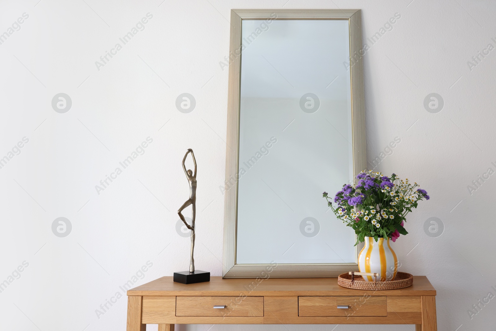 Photo of Beautiful flowers in vase and mirror on wooden table indoors