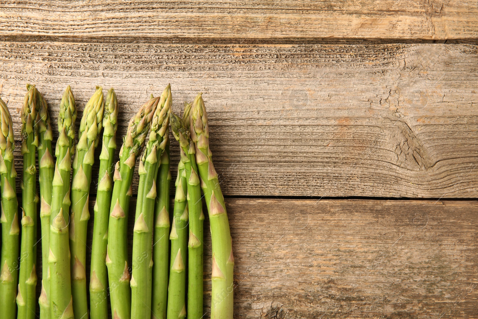 Photo of Fresh green asparagus stems on wooden table, flat lay. Space for text