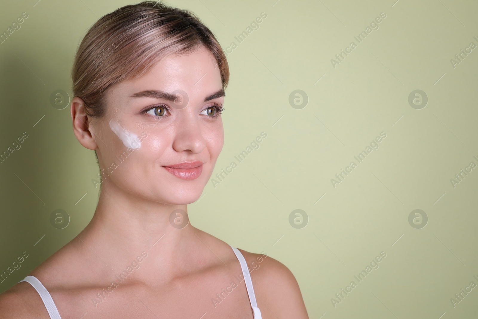 Photo of Beautiful woman with cream on her face against light green background, space for text