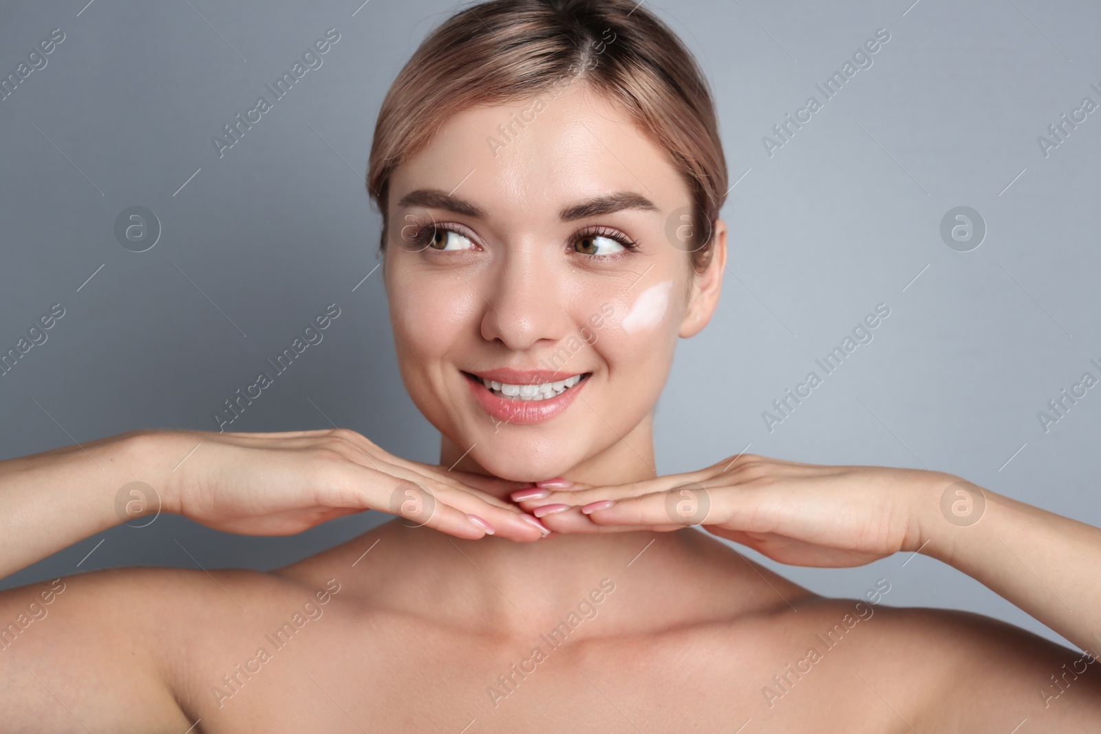 Photo of Beautiful woman with cream on her face against gray background