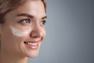 Photo of Beautiful woman with cream on her face against gray background, closeup. Space for text