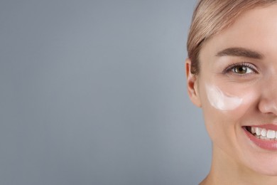 Photo of Beautiful woman with cream on her face against gray background, closeup. Space for text
