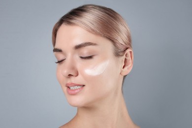 Photo of Beautiful woman with cream on her face against gray background, closeup