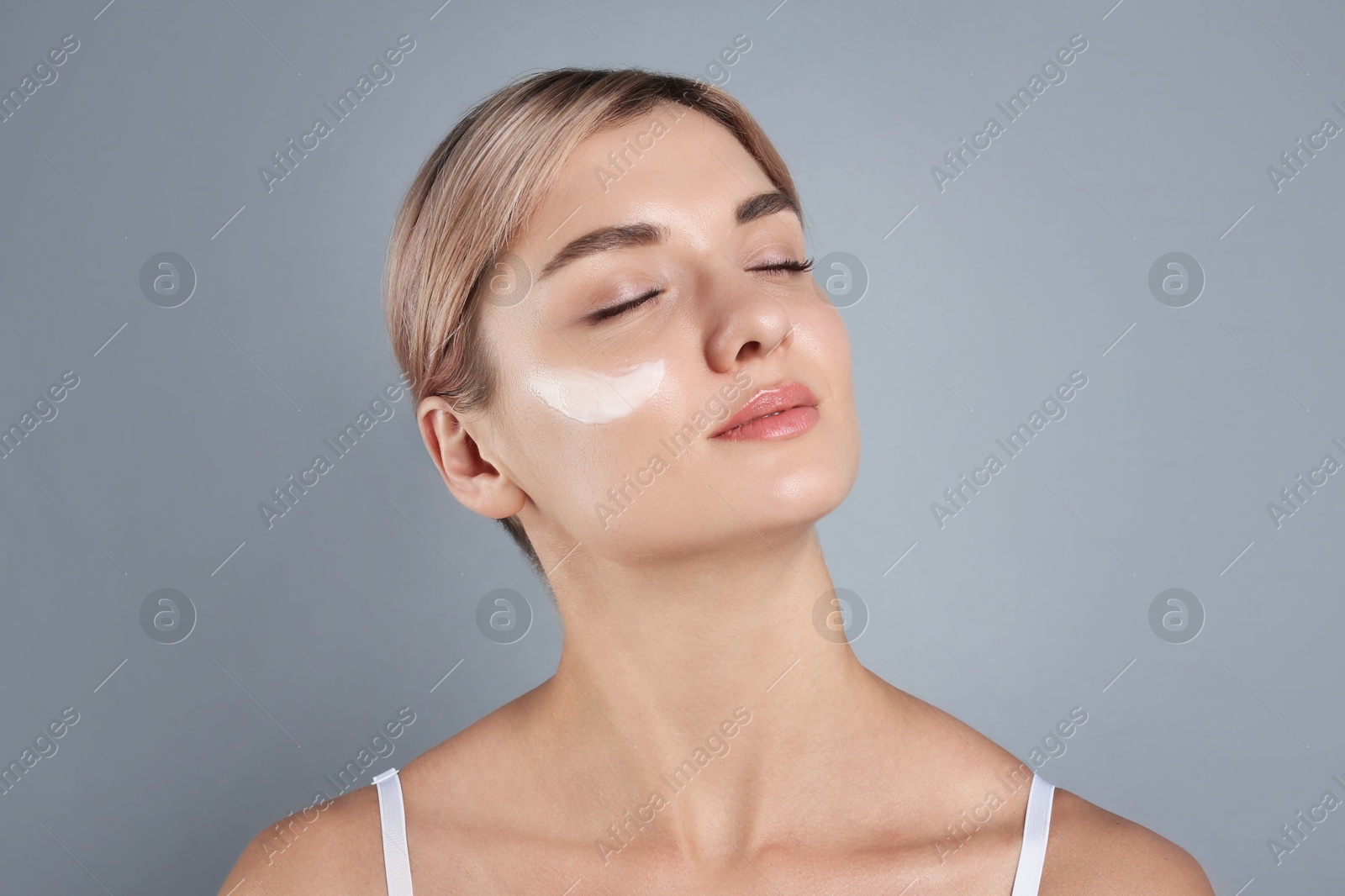 Photo of Beautiful woman with cream on her face against gray background