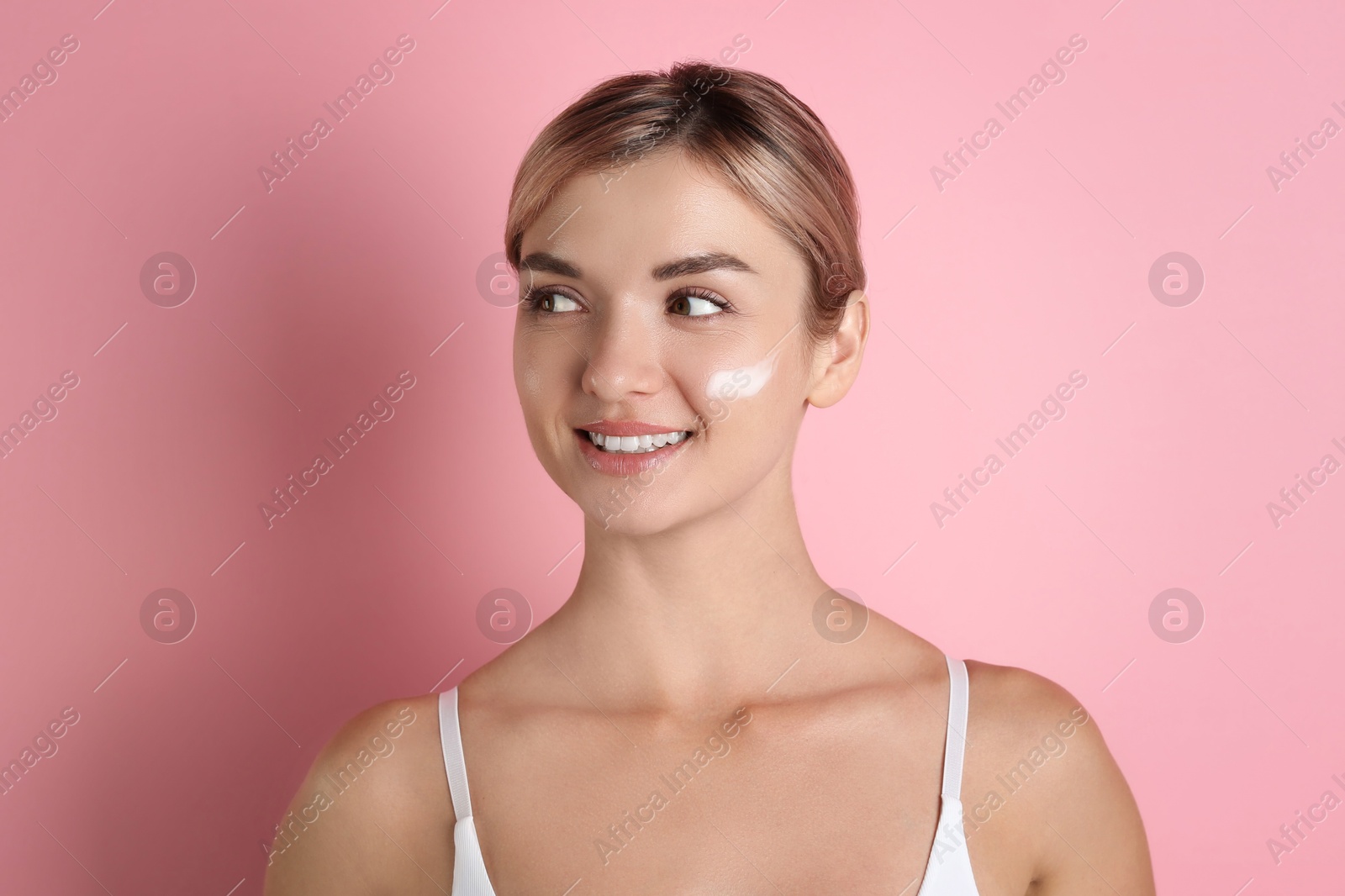 Photo of Beautiful woman with cream on her face against pink background