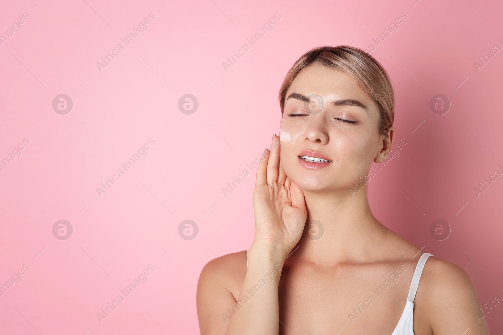 Photo of Beautiful woman with cream on her face against pink background, space for text