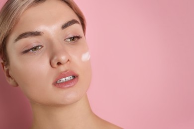 Photo of Beautiful woman with cream on her face against pink background, closeup. Space for text