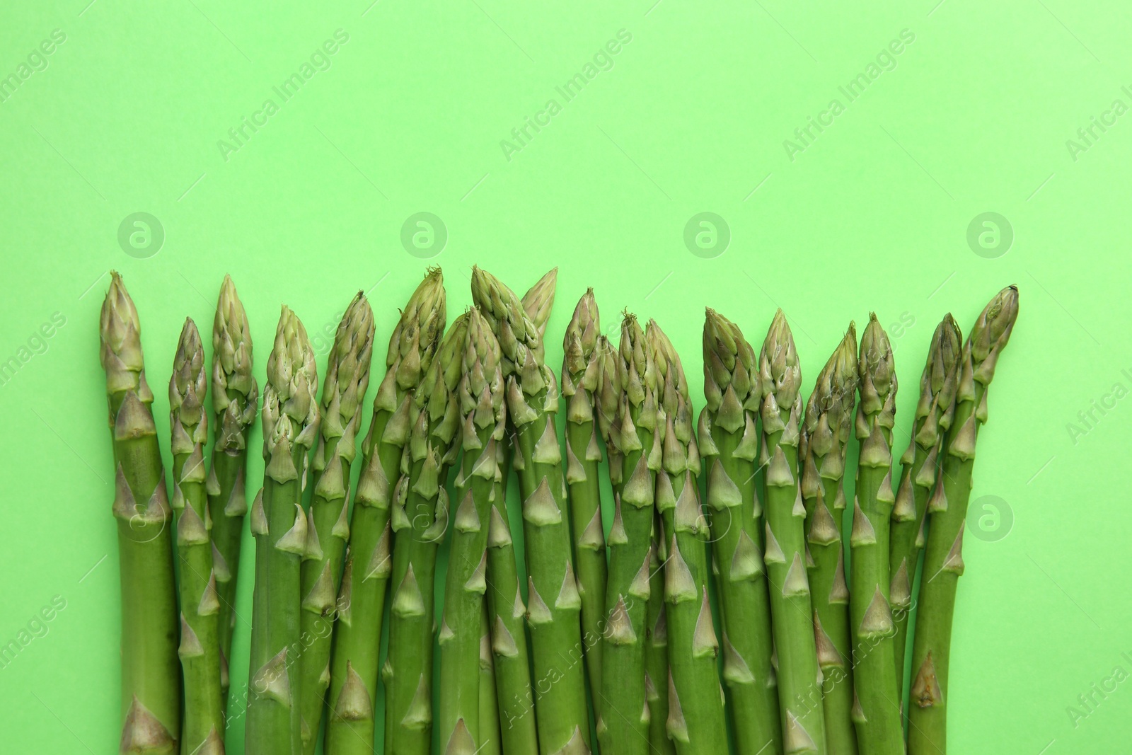 Photo of Fresh asparagus stems on green table, top view. Space for text