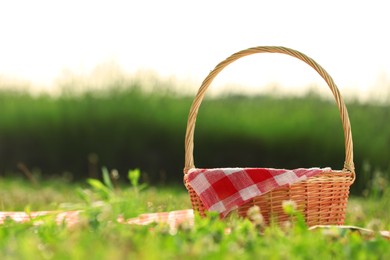 Photo of Picnic wicker basket with red checkered napkin and blanket on green grass outdoors, space for text