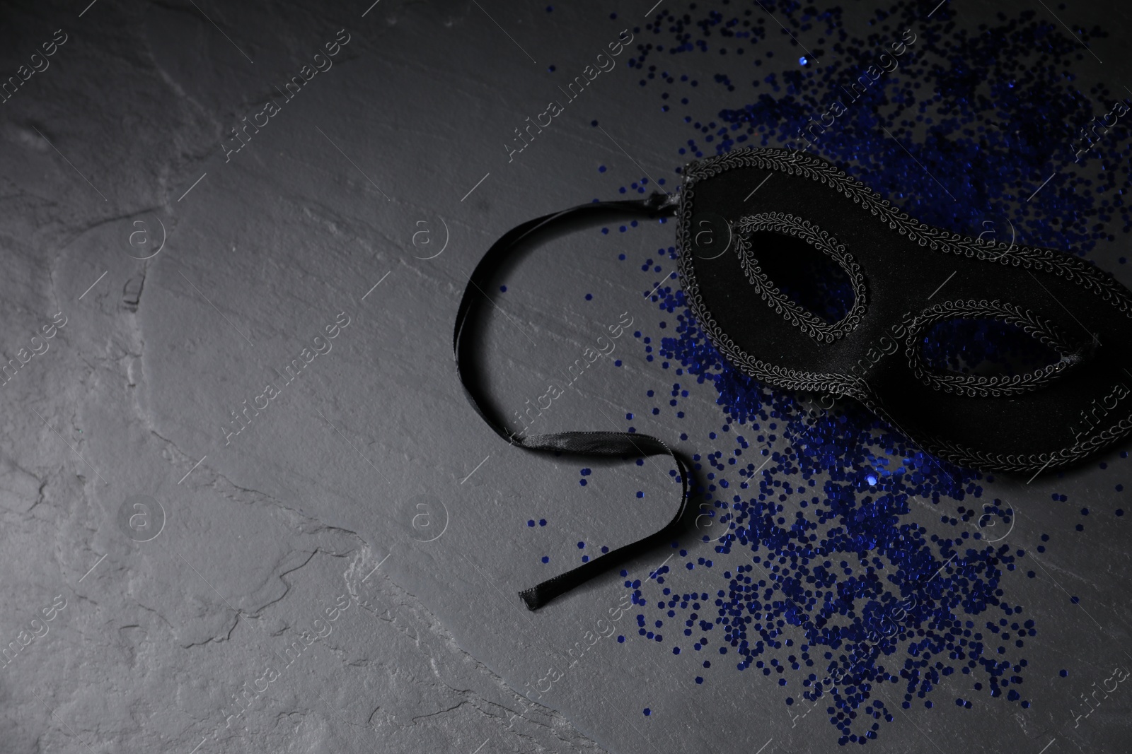 Photo of Beautiful carnival mask and blue sequins on black table. Space for text