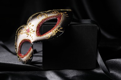 Photo of Beautiful carnival mask on black silk fabric, closeup